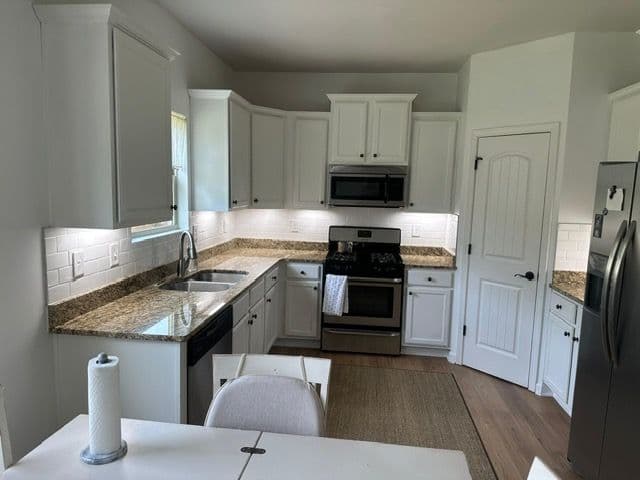 Modern kitchen with white cabinets, granite countertops, stainless steel appliances, and a dining area.