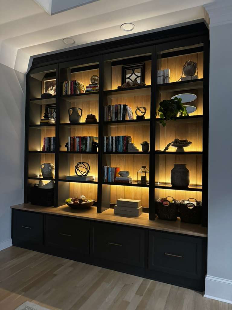 Modern black bookshelf with ambient lighting, displaying books, decor, and fruit.