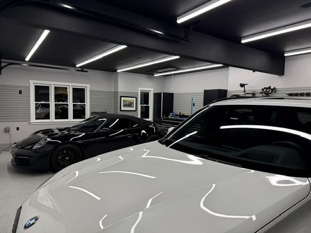 Luxury car garage featuring a sleek black sports car and a white vehicle under bright LED lights.