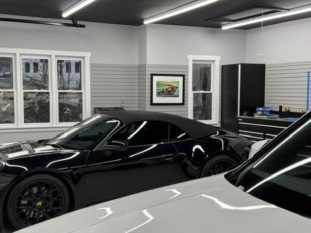 Sleek black sports car in modern garage with organized tools and wall art.