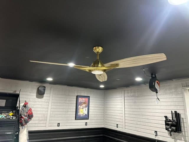 Modern ceiling fan with wooden blades and brass finish in a stylish black ceiling garage.