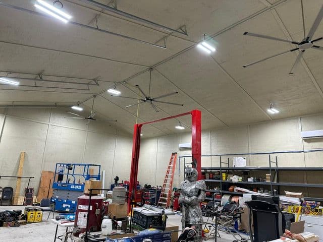 Spacious industrial workshop with equipment, large fans, and a red lift for vehicle maintenance.