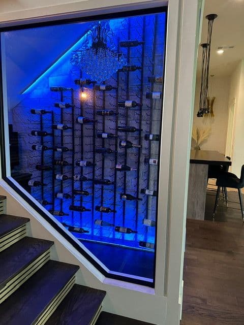 Modern wine cellar with illuminated racks, showcasing a variety of wine bottles behind glass.