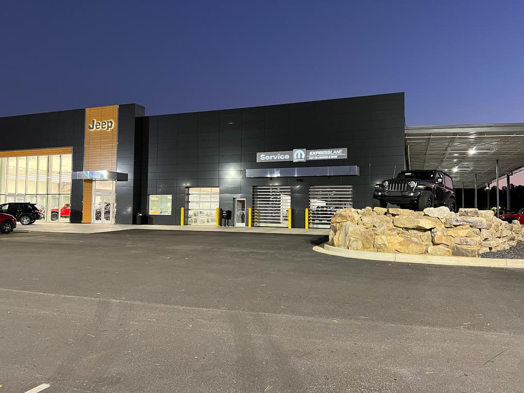 Jeep dealership exterior at twilight with service area and rock feature.