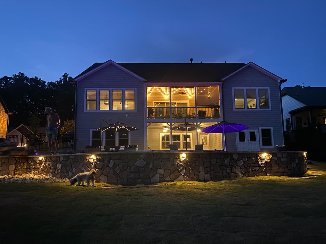 Modern house exterior at night, illuminated with string lights and outdoor seating.