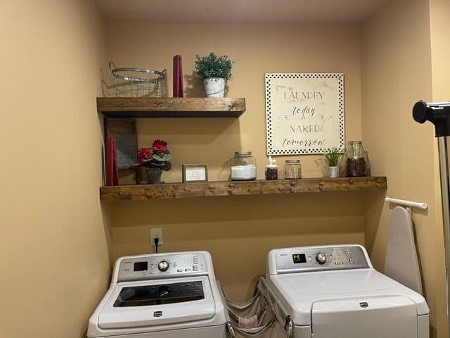 Modern laundry room with white washer and dryer, rustic shelves, and decorative baskets.