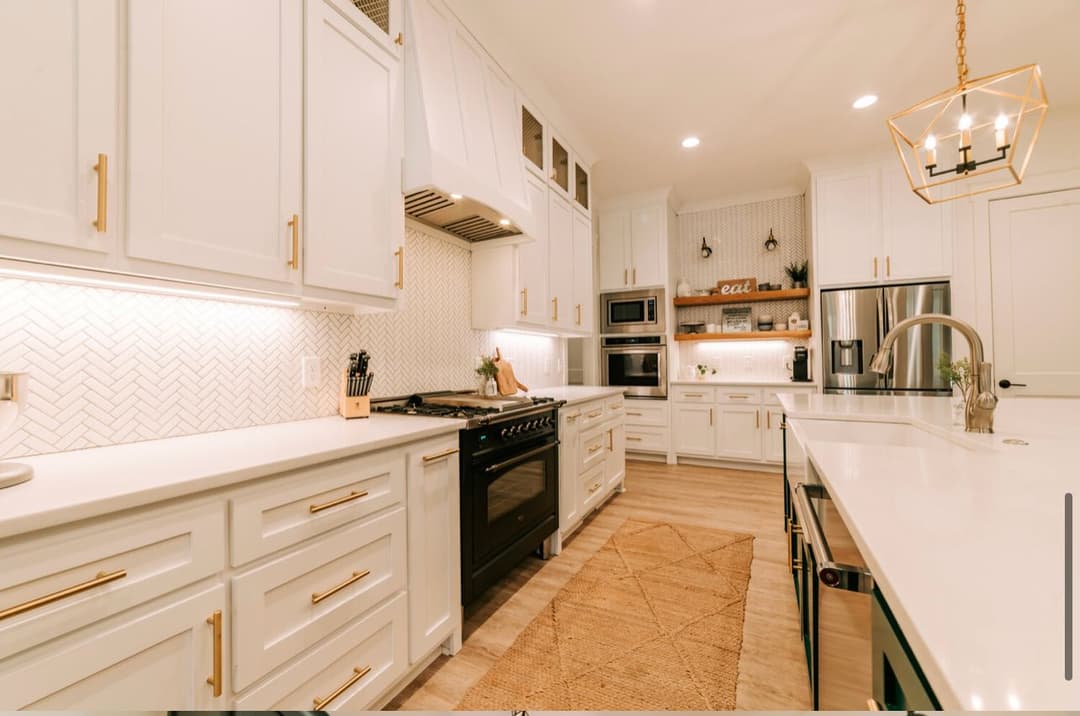 Modern kitchen with white cabinetry, herringbone backsplash, and stainless steel appliances.