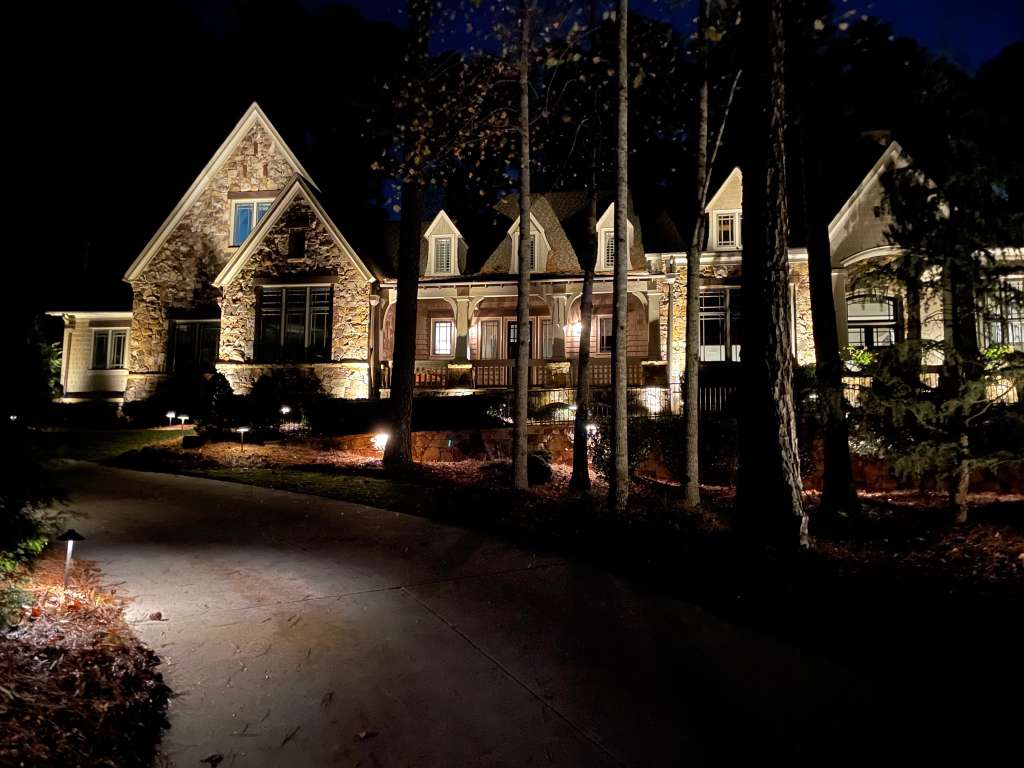 Elegant stone mansion illuminated at night, surrounded by trees and landscaped grounds.