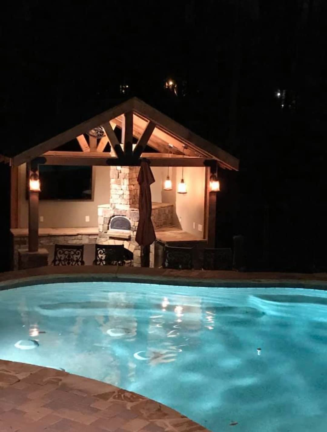Nighttime view of a backyard pool with a stone gazebo and subtle lighting.