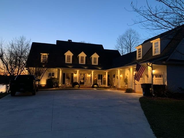 Beautiful house at dusk, warmly lit with an American flag and lake view in the background.