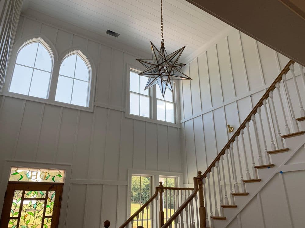 Bright entryway with star chandelier, white paneled walls, and staircase. Stained glass door visible.
