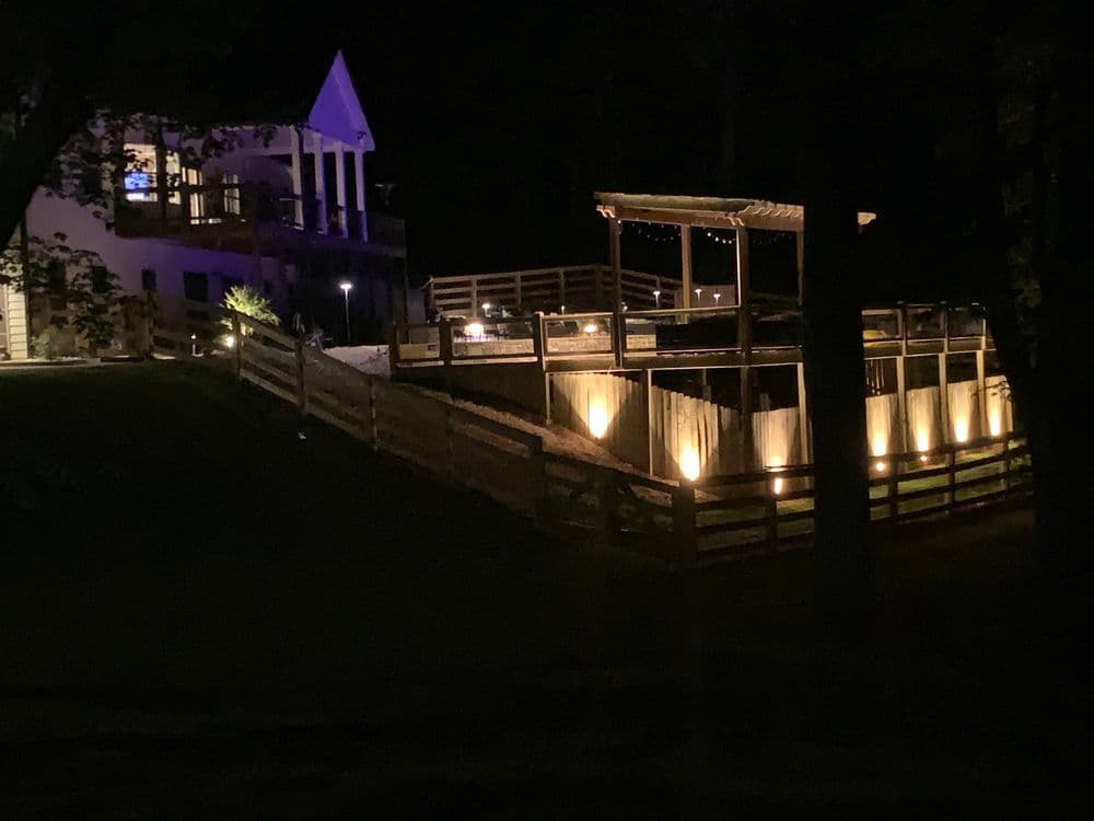 Lit outdoor deck and building at night, surrounded by trees and atmospheric lighting.