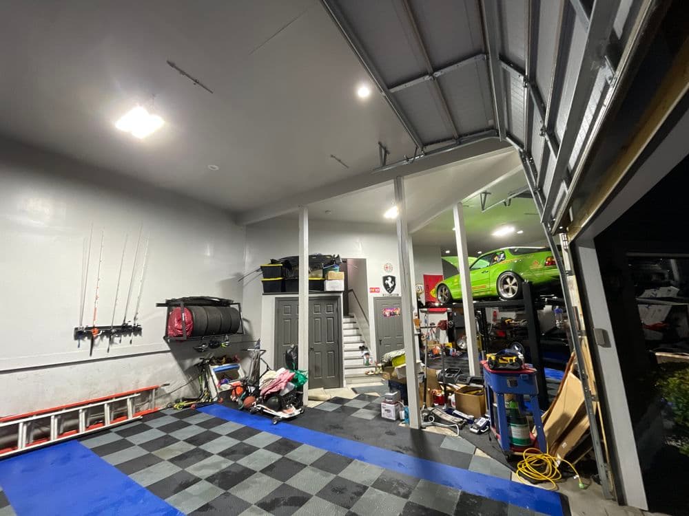 Spacious garage featuring a green sports car, storage, tools, and fishing gear.