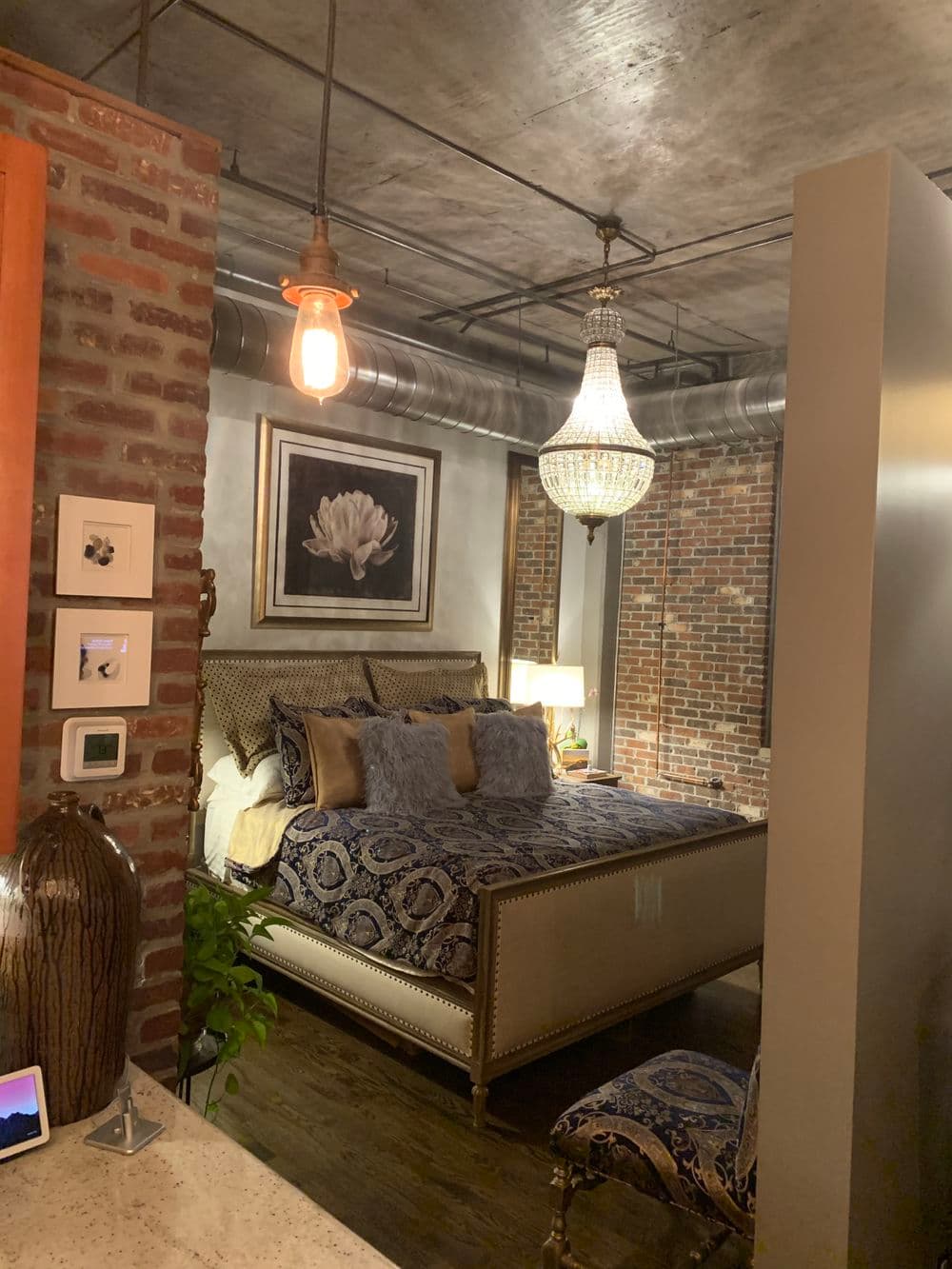 Cozy bedroom with brick walls, elegant chandelier, and luxurious bedding.