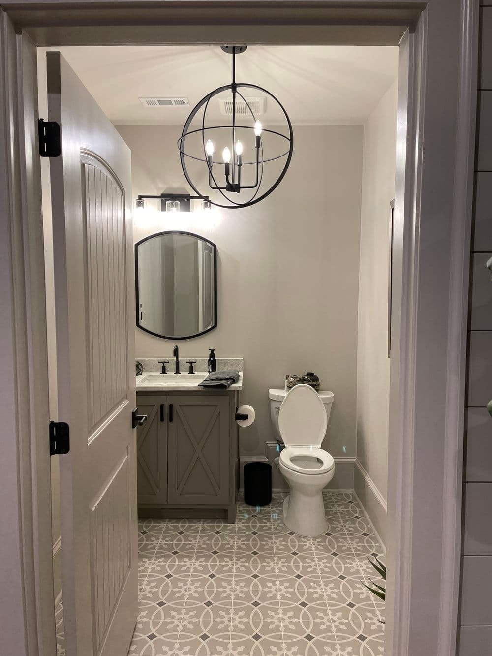 Modern bathroom with a stylish chandelier, gray cabinetry, and intricate floor tiles.